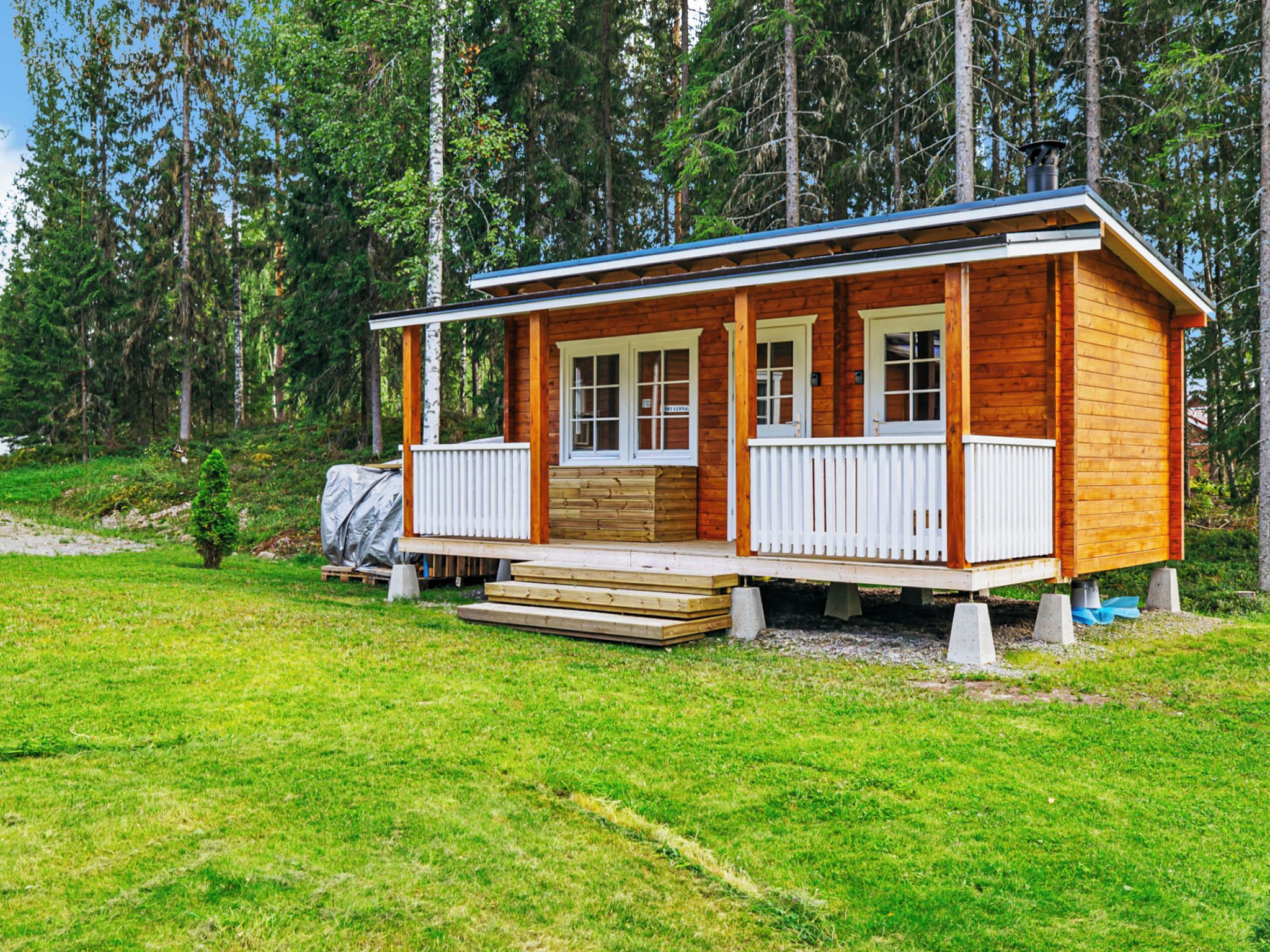 A wooden cabin with a porch, surrounded by a grassy area and trees.