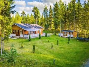 A cabin with a porch, a separate building with a deck, surrounded by a grassy yard and dense forest. - Aapeli iso by Interhome (Ähtäri)