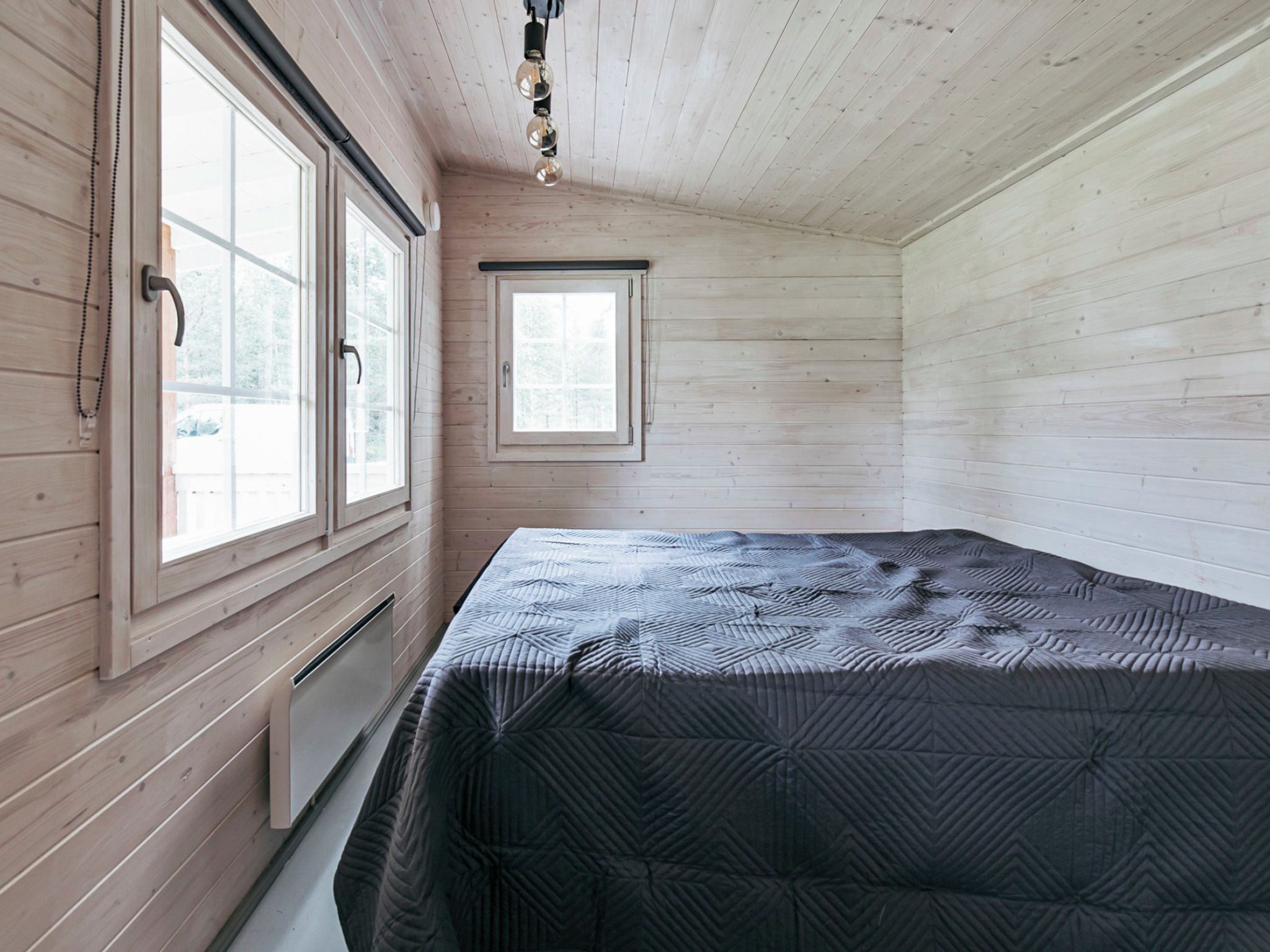Ein Zimmer mit einem Bett, zwei Fenstern und einer Heizung.