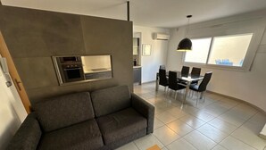 A modern living room with a grey sofa, a wooden coffee table, and a dining area with a table and chairs. - Drugstore A A - Two Bedroom Apartment, Sleeps 6 (Roses)