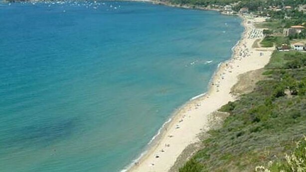 Una zona costanera amb una platja, un petit poble i turons al fons.