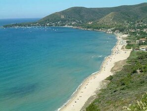 Un paysage côtier avec une plage, une petite ville et des collines en arrière-plan.