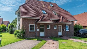 Une maison à deux étages, construite en briques, avec un toit recouvert de tuiles rouges, une porte d’entrée et une allée pavée.