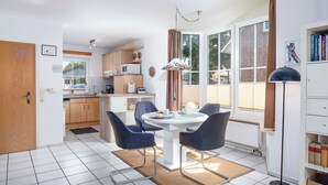 Une cuisine moderne avec des meubles blancs, un coin repas doté d’une table ronde et de chaises, et une grande fenêtre avec des rideaux.