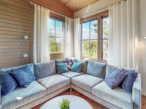 A corner living room with a sectional sofa, two windows with curtains, and a small plant on a white coffee table.