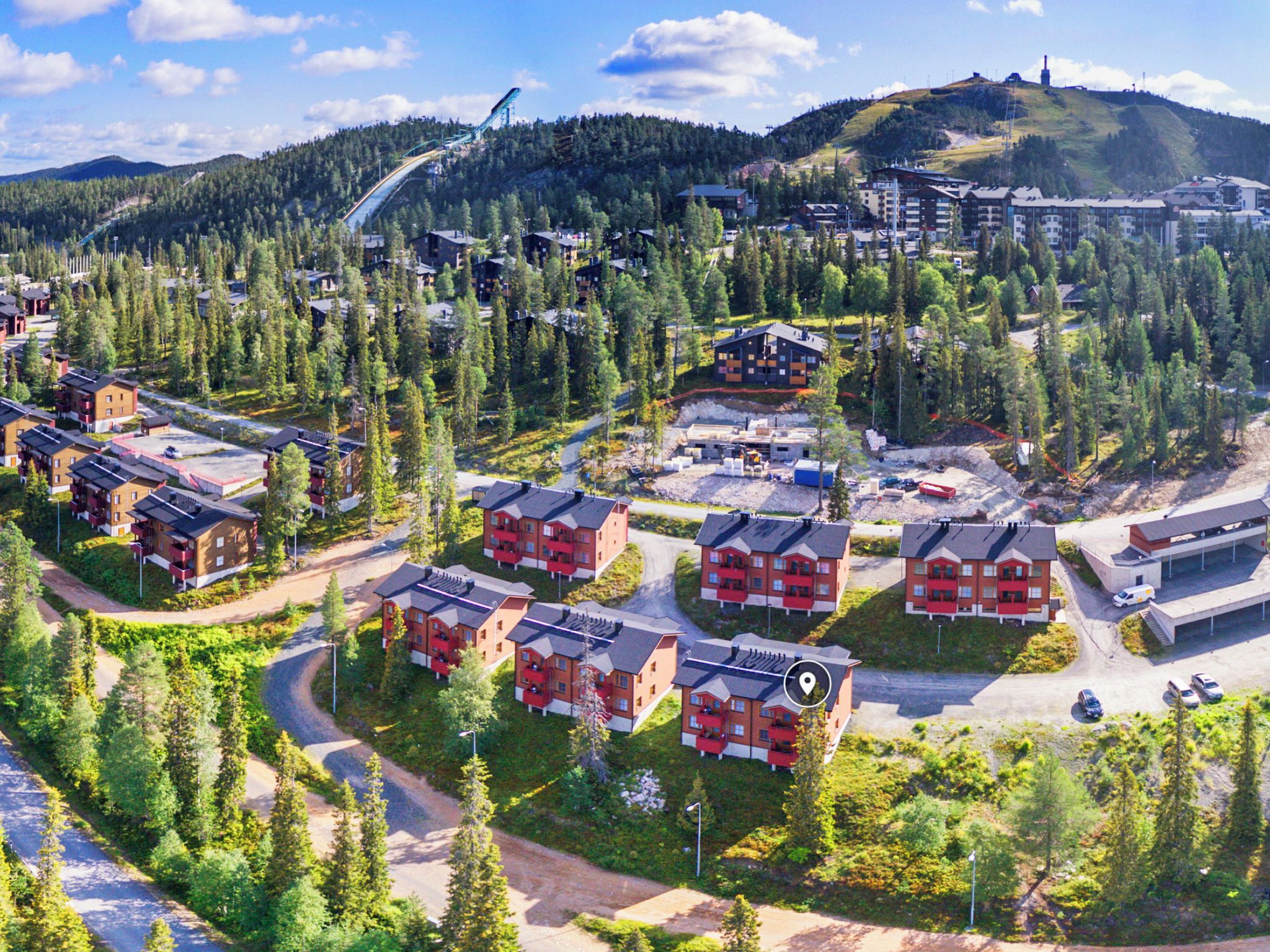 A residential area with multiple red buildings, roads, and a ski lift in the background.