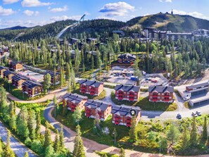 A residential area with multiple red buildings, roads, and a ski lift in the background.