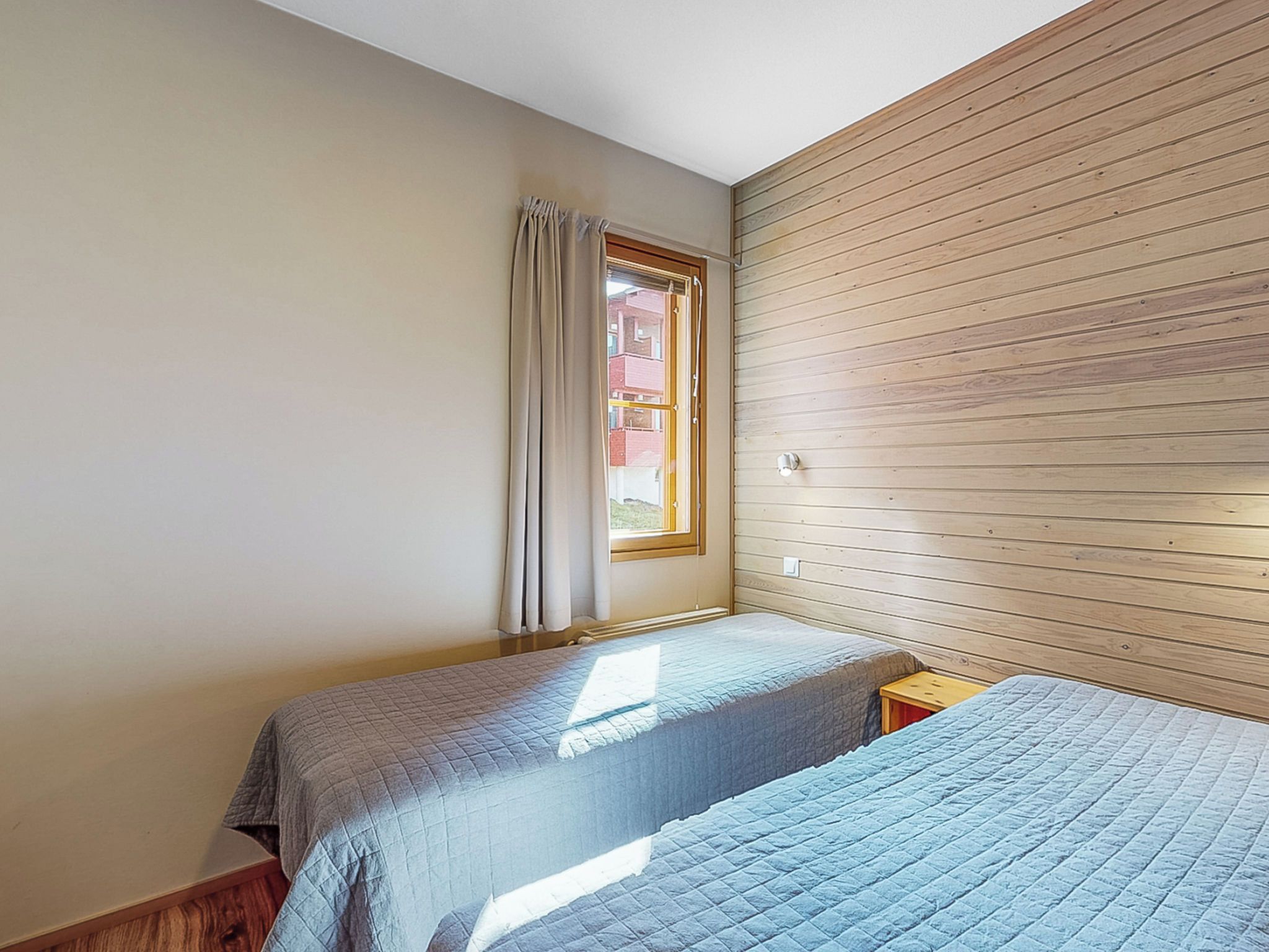 Una habitación con dos camas, una ventana con cortinas y paneles de madera en una pared.