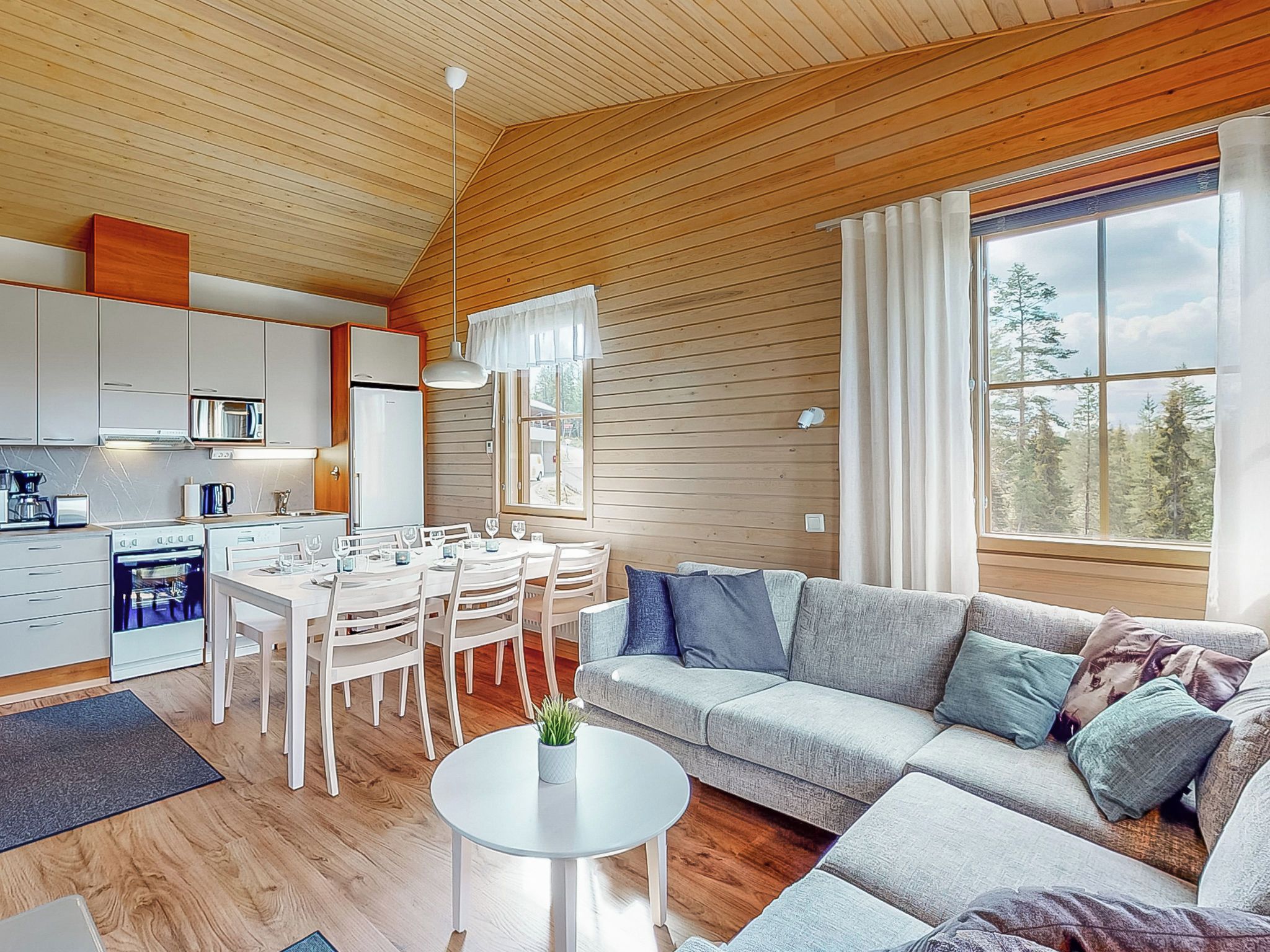 Ein modernes Interieur mit Essbereich, Küche und einem großen Fenster mit Blick auf Bäume.