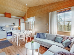 Un interior moderno con comedor, cocina y un amplio ventanal con vista a árboles.