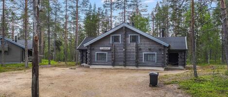 A log cabin with a clear sky, surrounded by tall trees.