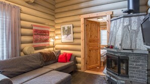 Ein gemütliches Blockhaus-Interieur mit einer Couch, einem Kamin und einer Holztür, die in einen anderen Raum führt.