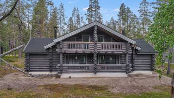 A log cabin with a central balcony, surrounded by a forest.