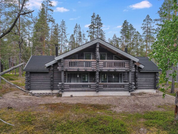 A log cabin with a central balcony, surrounded by a forest.
