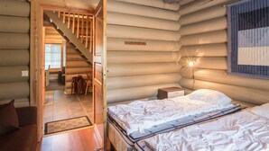 Ein gemütliches Blockhauszimmer mit einem Bett, einem Nachttisch und einer Holztreppe, die zu einem anderen Raum führt.
