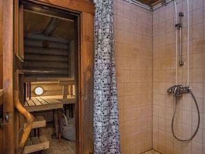 Uma sauna de madeira com banco e luminária pendente, área de chuveiro com mangueira e cortina estampada.
