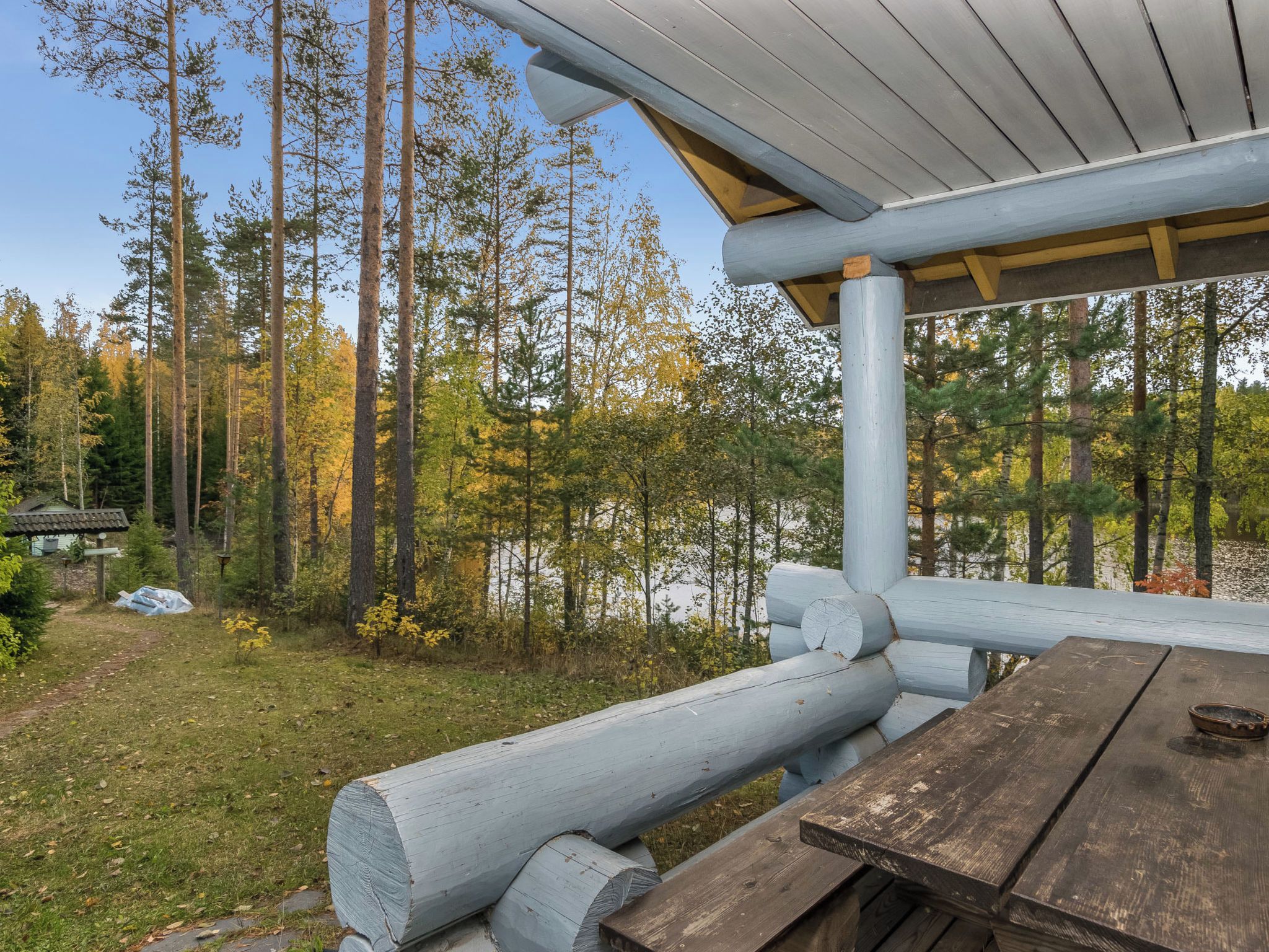 Ein Holztisch mit Bänken in einem bewaldeten Gebiet, blauer Himmel.