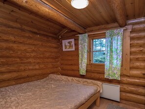 A wooden cabin room with a bed, a window with curtains, and a radiator. - Harrila by Interhome (Mikkeli)