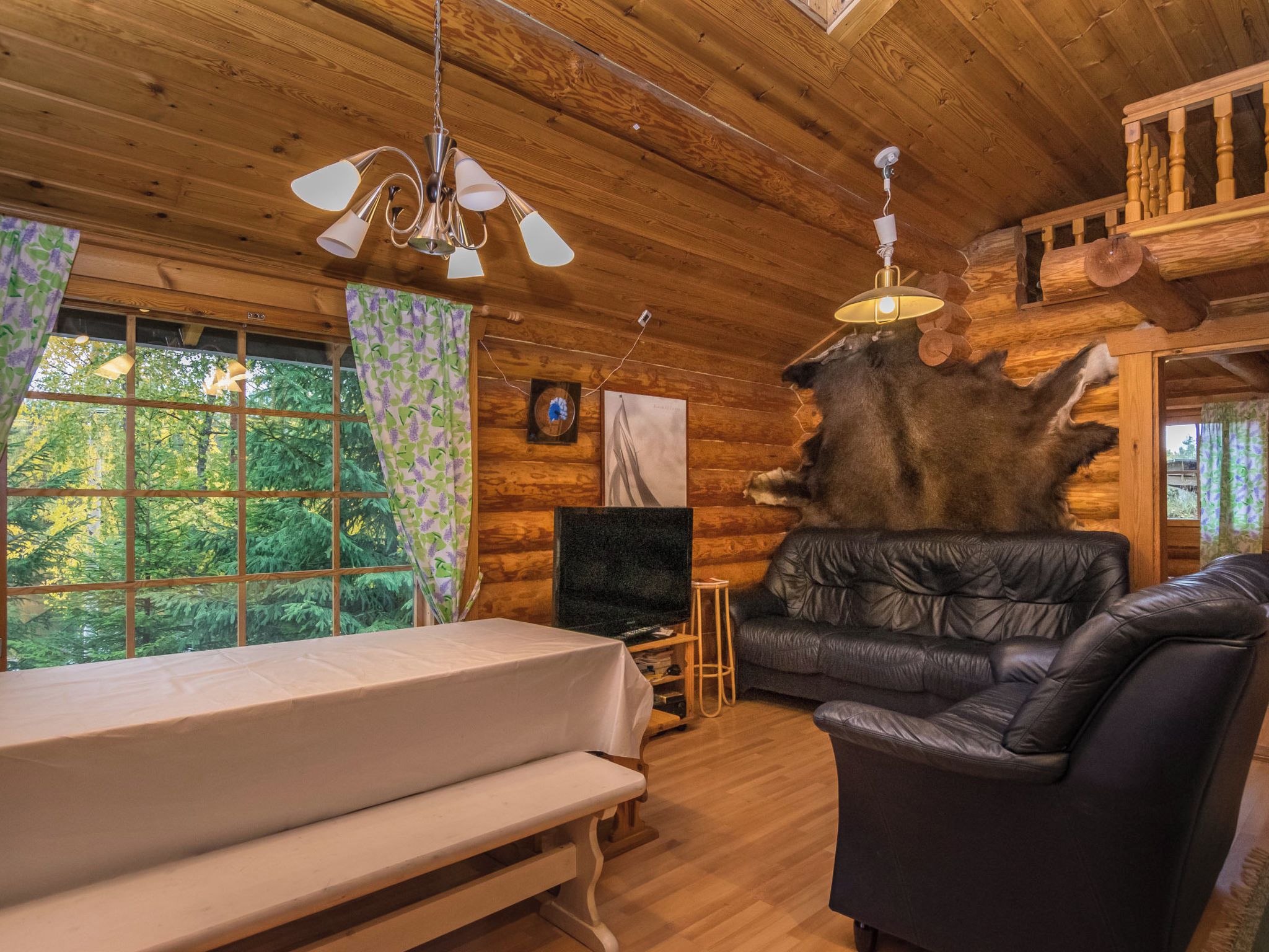 Interior de una cabaña de troncos con una cama, un sofá de cuero y un trofeo de piel de animal.