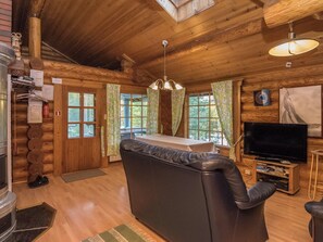 Interior de una cabaña de madera con sofá, televisión y zona de comedor.