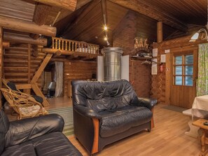 A cozy log cabin interior with a leather sofa, a wicker chair, and a wooden staircase. - Harrila by Interhome (Mikkeli)