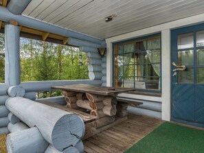 A log cabin with a wooden table and benches, a blue door, and a window with curtains.