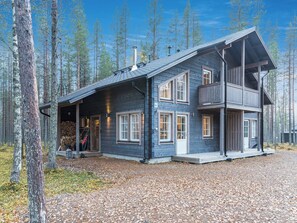 Eine zweistöckige Holzhütte mit einem Balkon, umgeben von einem Wald.