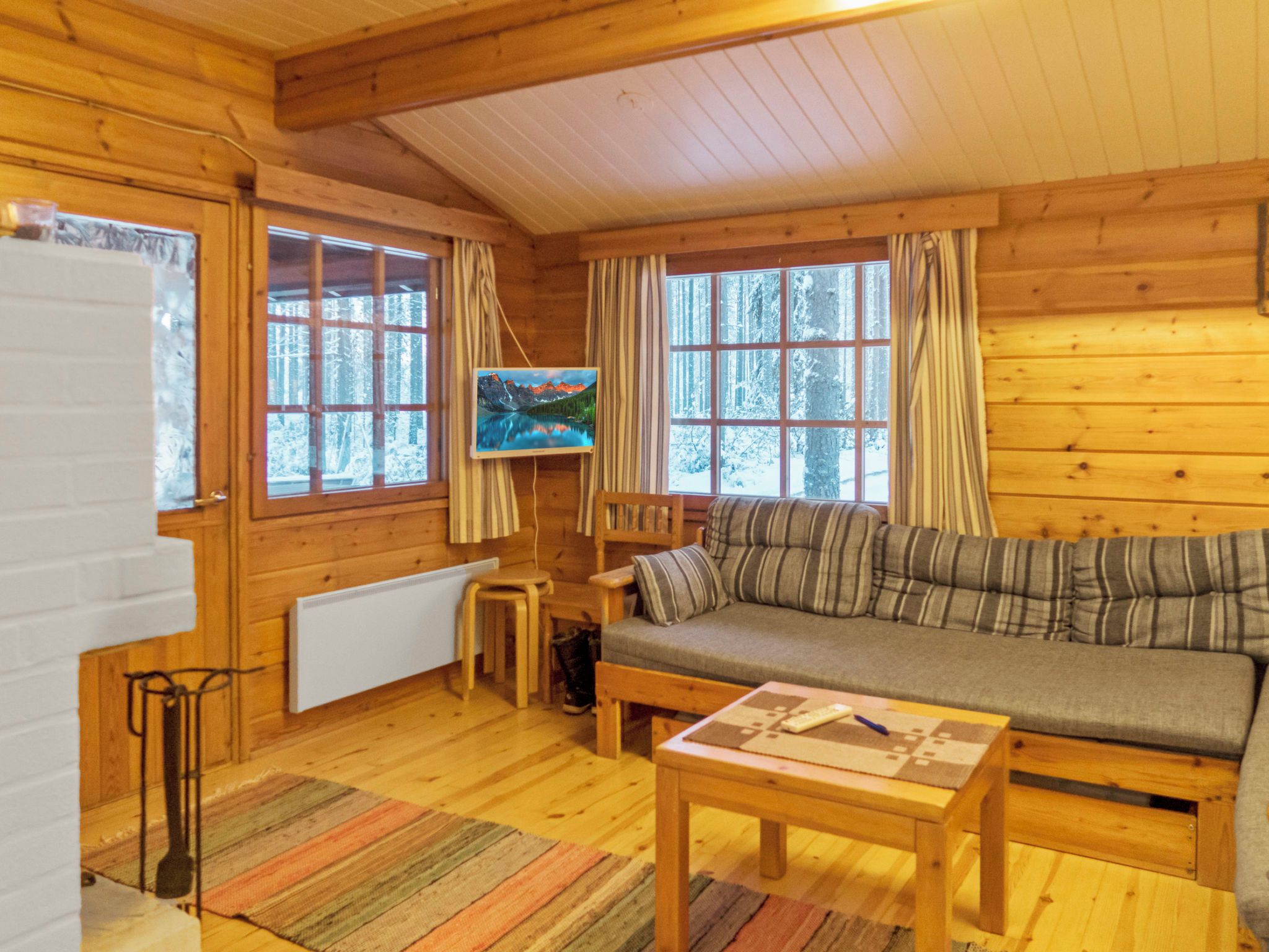 A cozy cabin interior with a wooden floor, a sofa, a small table, and two windows with curtains.