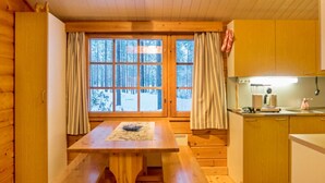 A wooden cabin with a dining table and benches, a kitchen area, and a window with curtains. - Kanerva by Interhome (Sotkamo)