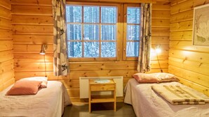 A cozy cabin room with two beds, a small table, and a window with a view of a snowy forest. - Kanerva by Interhome (Sotkamo)