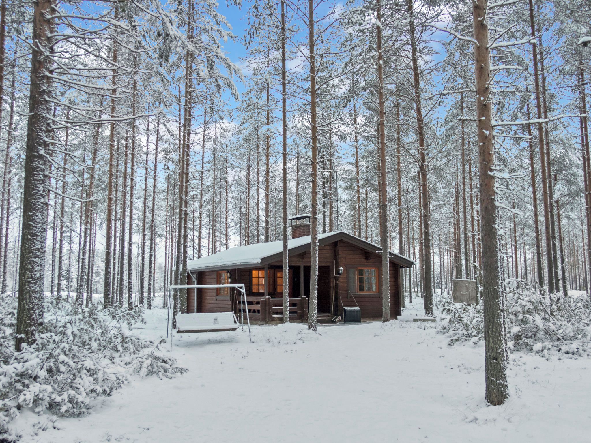 A cabin in a snowy forest with a porch and a chimney.