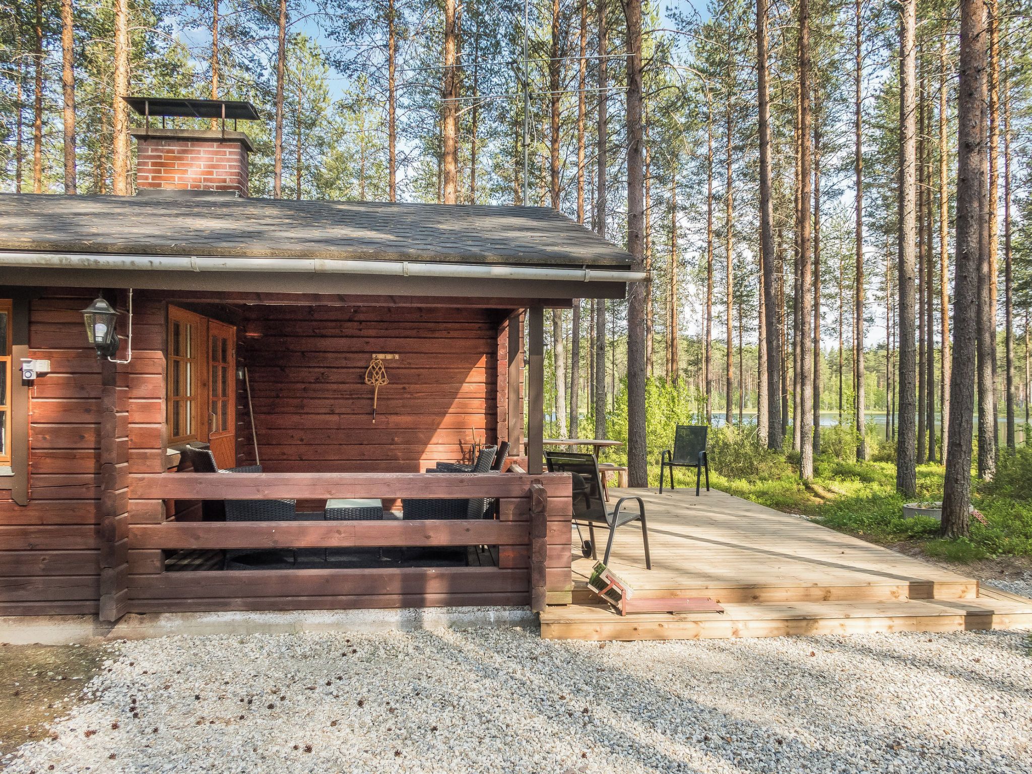 A wooden cabin with a porch, a chimney, and a gravel driveway leading to a dock.