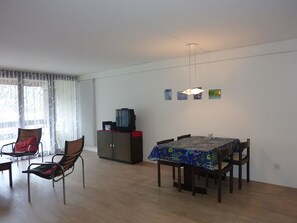 A dining area with a table set for four, a cabinet, and a chair with a red cushion.