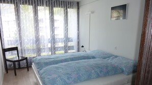 Een slaapkamer met een bed, een stoel, een nachtkastje en een raam met gordijnen.