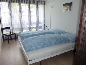 A bedroom with a bed, a chair, a bedside table, and a window with curtains. - Neuschwändi 5 Appartement/Fewo 4-Bettwohnung by Interhome (Engelberg)