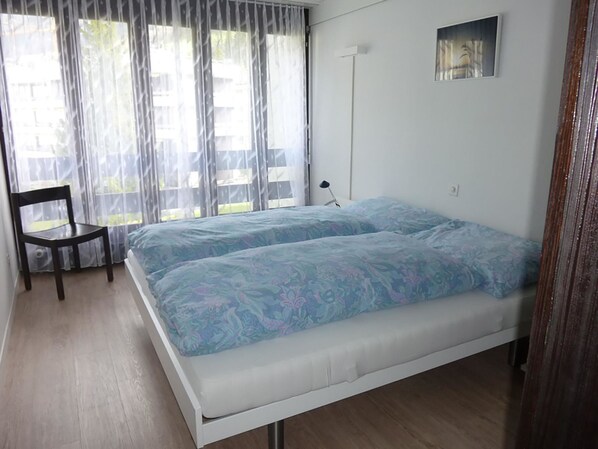 A bedroom with a bed, a chair, a bedside table, and a window with curtains.