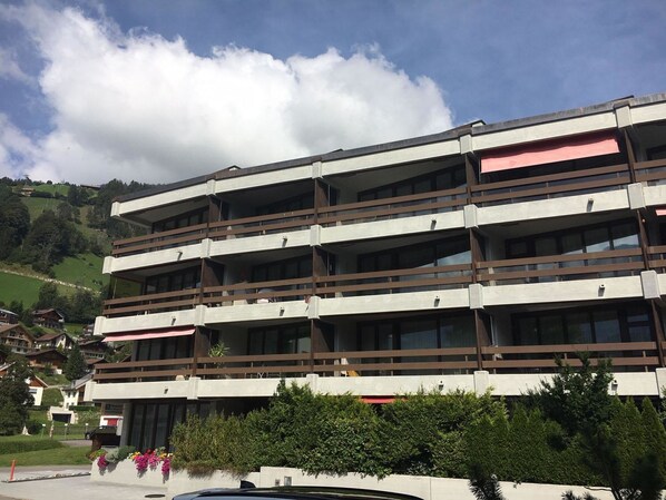 A multi-story hotel with balconies, a parking area, and a view of the surrounding landscape.