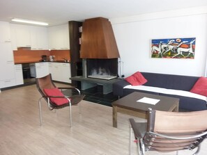 A modern living room with a sofa, a dining table, and a chair. There is a fireplace and a kitchen in the background. - Neuschwändi 5 Appartement/Fewo 4-Bettwohnung by Interhome (Engelberg)