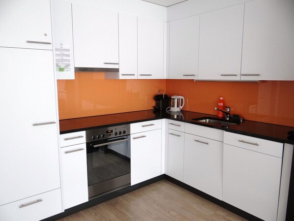 Een koelkast, een oven, een vaatwasser, kookgerei, borden en bestek