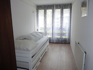 A bedroom with a bed, a window with curtains, and a radiator.