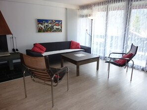 A modern living room with a sofa, a coffee table, and a chair. There is a painting on the wall and a window with curtains.