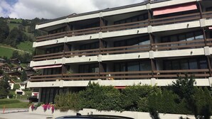 Een meerlaags gebouw met balkons, omgeven door groen en een glooiend landschap.