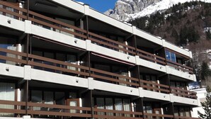 Een meerhoog hotel met balkons, gelegen voor een berglandschap met sneeuwtoppen.