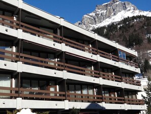 A multi-story hotel with balconies, set against a backdrop of snow-capped mountains.