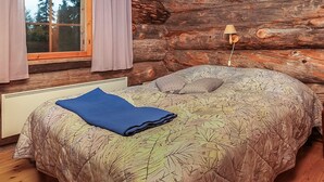 Een slaapkamer in een blokhut met een bed, raam en houten wanden.