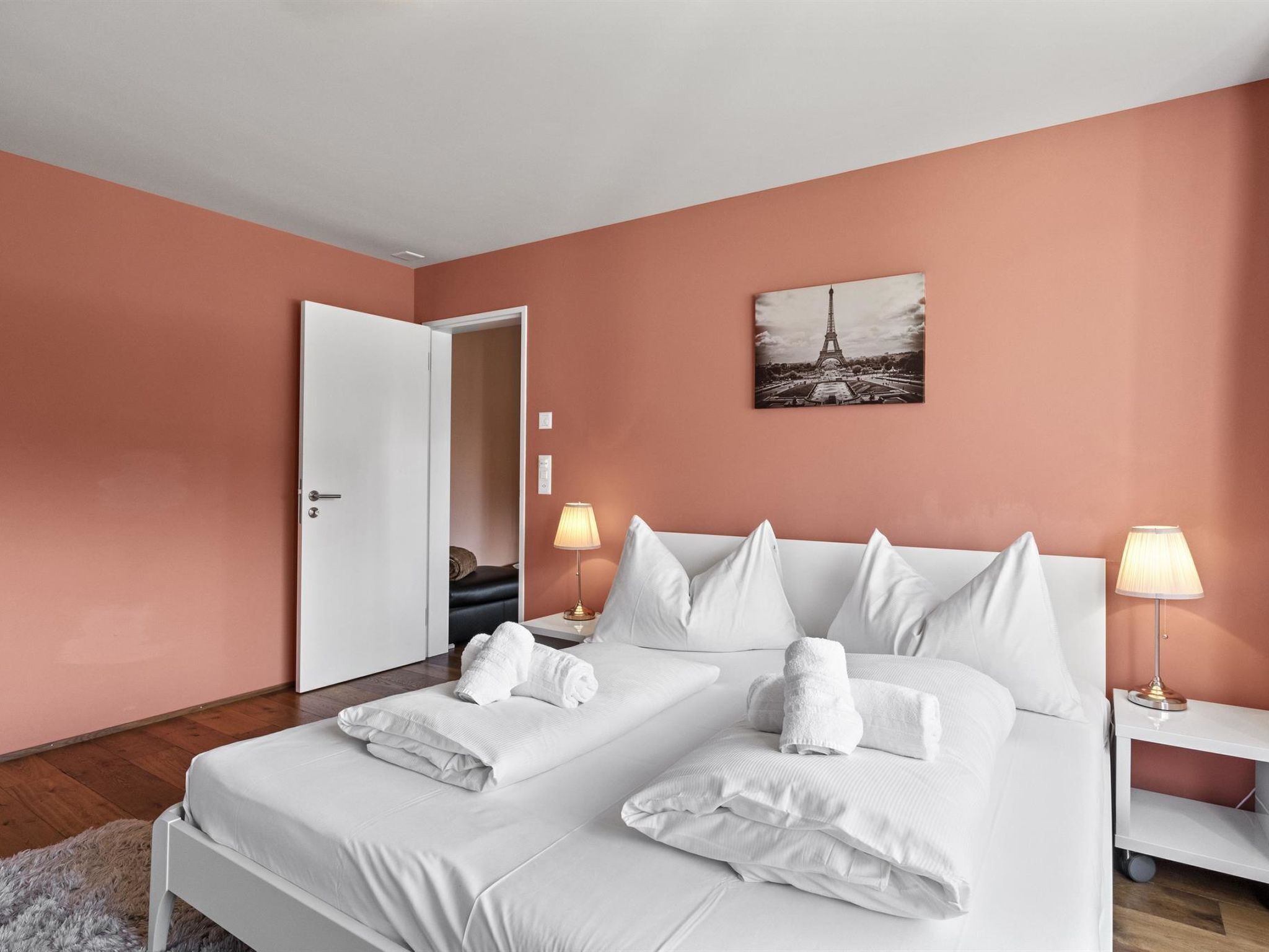 Quarto de hotel com duas camas, roupa de cama branca, um quadro da Torre Eiffel e luminárias de cabeceira.