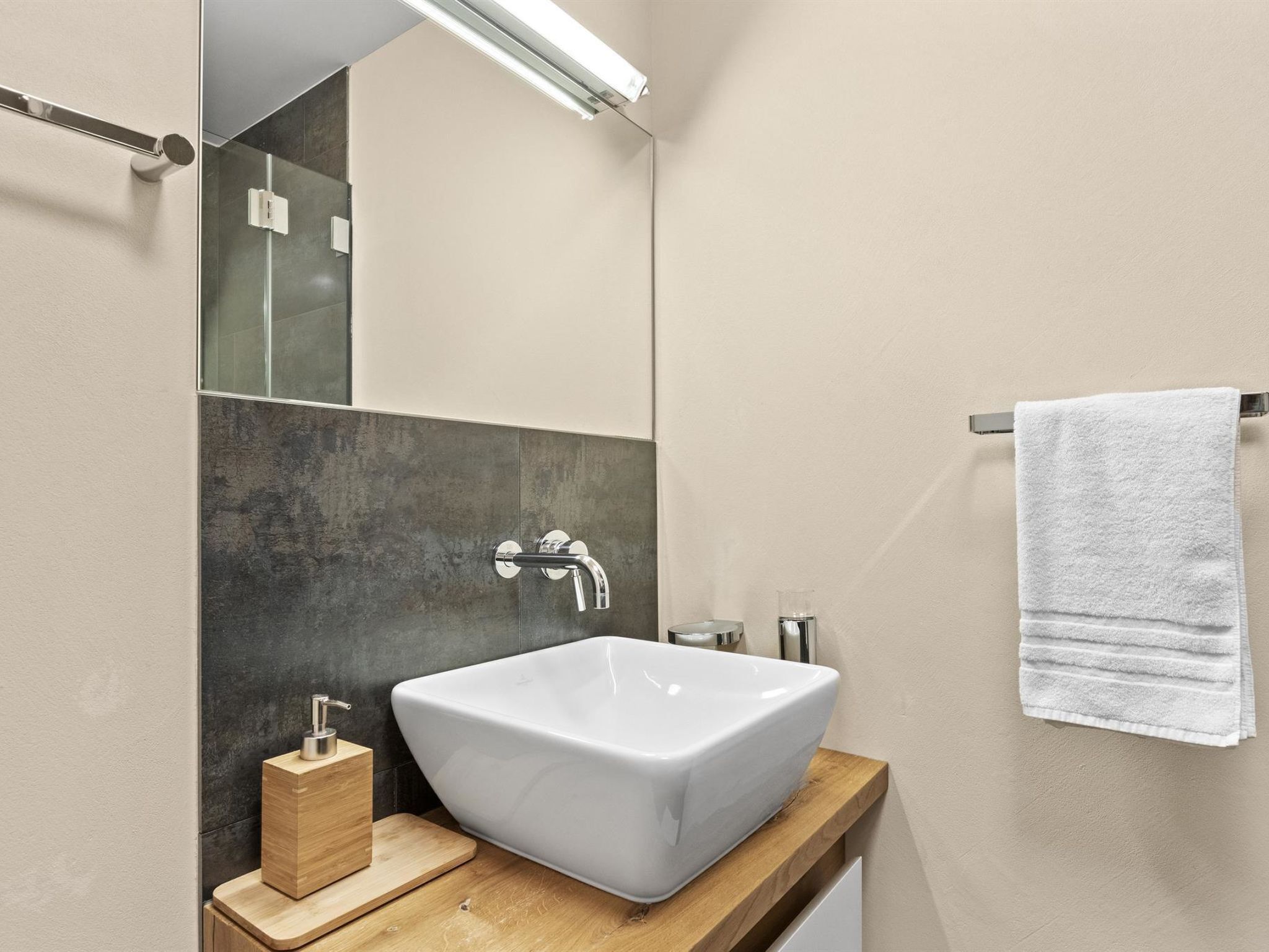 A modern bathroom with a large white vessel sink, a wooden vanity, a mirror, and a towel rack.