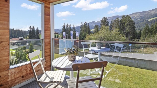 Un balcon en bois doté d’une rambarde en verre, offrant une vue sur un paysage montagneux.