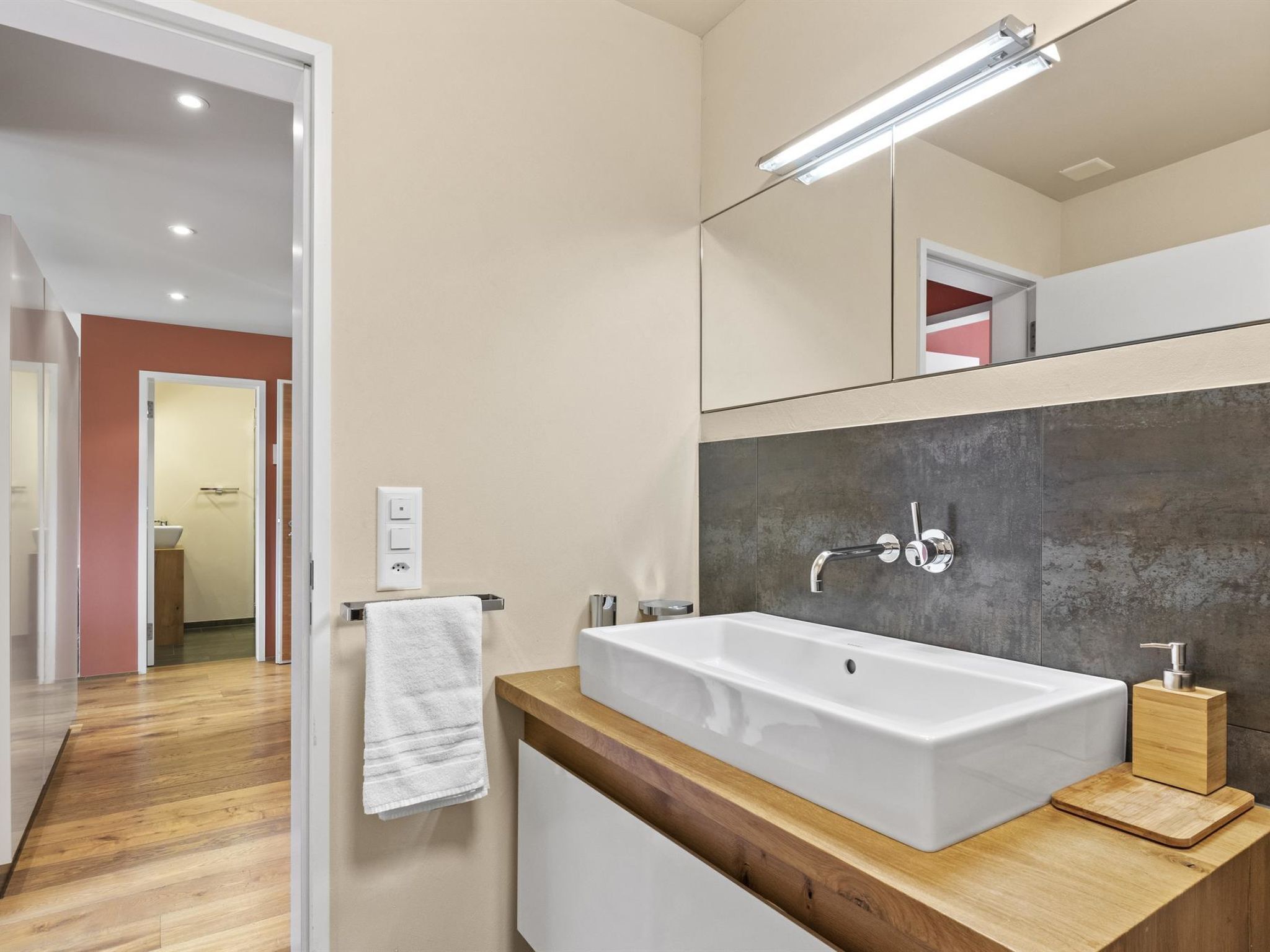 A modern bathroom with a large white sink, wooden countertop, and a mirror above the sink.