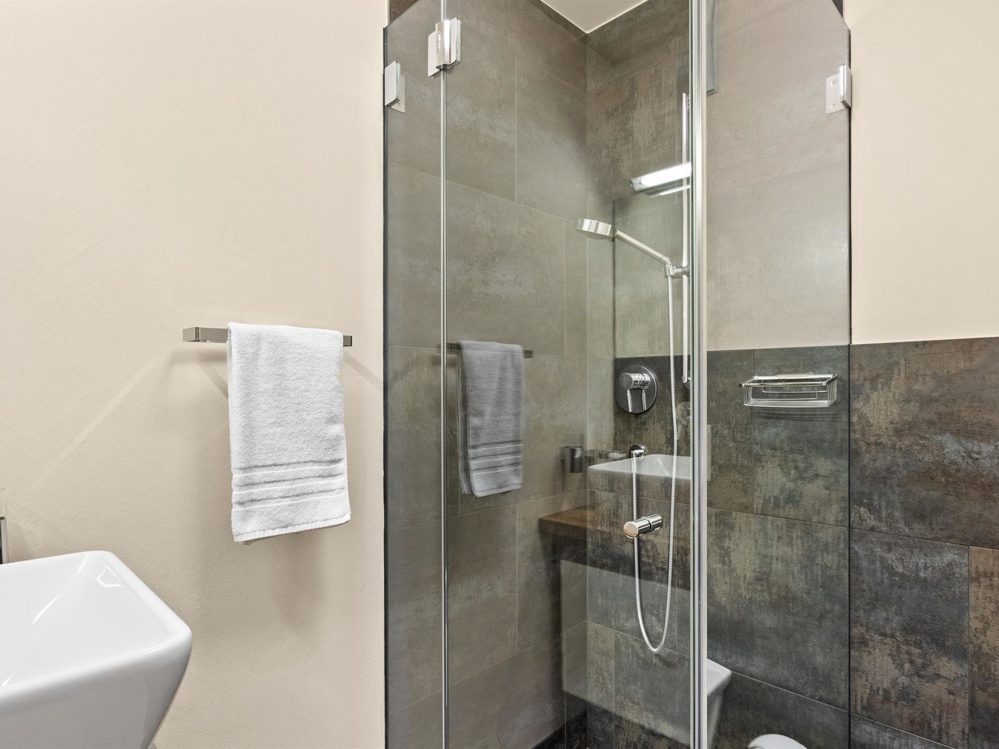 Un bagno moderno con doccia vetrata, lavandino bianco e porta asciugamani.